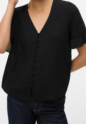 Schwarze Bluse mit kurzen Ärmeln, stoffbezogenen Knöpfen vorne und V-Ausschnitt, getragen zu dunkelblauen Jeans.