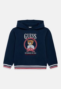 Φούτερ με κουκούλα σε ναυτικό μπλε χρώμα με γραφικό αρκούδας στο μπροστινό μέρος, κόκκινα και λευκά κεντημένα στοιχεία, συμπεριλαμβανομένου του "GUESS" και ριγέ τελείωμα. Υλικό από βαμβακερό μείγμα.