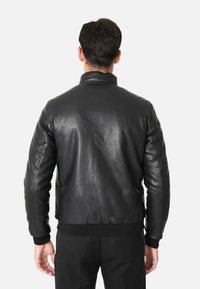 Giacca bomber in pelle nera con colletto e polsini a coste, caratterizzata da una texture liscia e un design pulito e semplice.