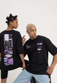 Black oversized t-shirts with purple graphic designs. One features text and symbols on the back; the other has a small design on the front.