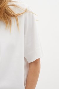 Hvid bomulds T-shirt med afslappet fit, korte ærmer og glat tekstur, der har en subtil sideslidsdetalje nær kanten.