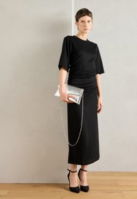 Μαύρο, εφαρμοστό φόρεμα με κοντά μανίκια και συγκεντρωμένη λεπτομέρεια στη μέση. Συνδυασμένο με ασημένια μεταλλική τσάντα με αλυσίδα και μαύρες ψηλές γόβες.