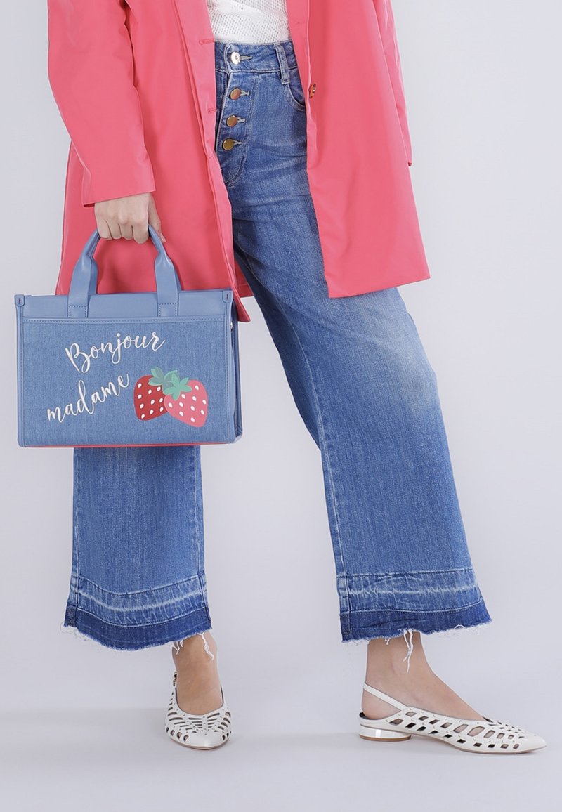 Femme portant un jean large bleu et un manteau rose, tenant un sac à main bleu avec le texte "Bonjour madame" et des illustrations de fraises.