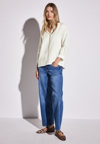 Blouse en lin beige clair avec un col en V et des manches trois-quarts, associée à un jean droit bleu et des ballerines imprimé léopard.