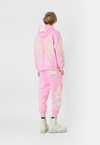 Sudadera rosa y pantalones de chándal a juego con grandes gráficos de alas. El conjunto está hecho de un material suave y se combina con botas de colores claros.