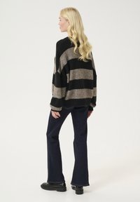 Maglione oversize a righe in nero e taupe, realizzato in morbido tessuto testurizzato. Abbinato a jeans svasati scuri e mocassini neri.