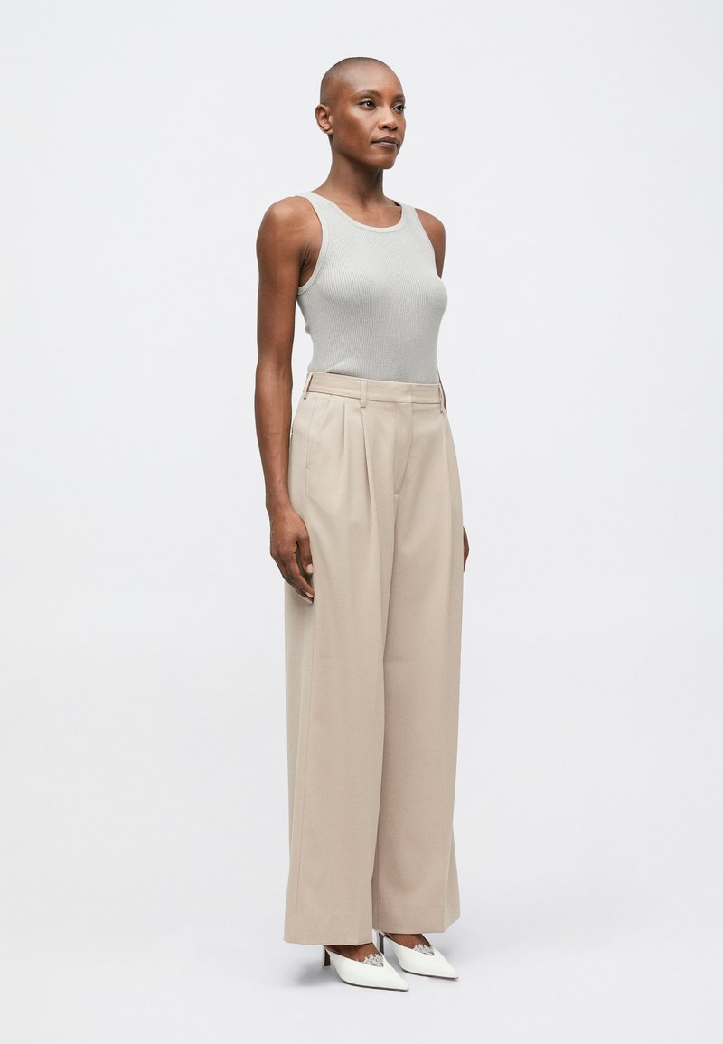 Top de tirantes gris acanalado combinado con pantalones beiges de talle alto y pliegues, y tacones blancos de punta afilada. Diseño minimalista y corte ajustado.