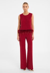 Rood tweedelig outfit met een mouwloze top met een verenrand en flared broek, gemaakt van een glinsterende stof.