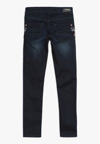 Tmavě modré džíny skinny s hladkým povrchem, pěti kapsami a dekorativním šitím na zadní kapse. Součástí jsou stříbrné kovové detaily.