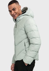 Helle grüne Nylonpuffjacke mit Kapuze, diagonal gesteppten Paneelen, Frontreißverschluss und seitlichen Taschen. Glatte, glänzende Textur.