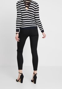 Pruhovaný svetr v námořnické modři a bílé s detailem otevřených zad, v kombinaci s černými úzkými džínami a černými lodičkami na podpatku.