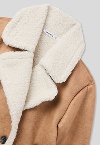 Giacca in suede marrone finta con collo in pile crema e superficie testurizzata. Presenta una chiusura con bottoni e un interno morbido e accogliente.