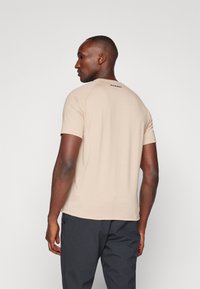 Jasnobeżowy t-shirt z krótkim rękawem, okrągłym dekoltem i rękawami raglanowymi. Posiada subtelną markę na górnej części pleców. Miękka faktura materiału.