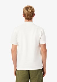 Vit polo skjorta med mjuk textur, korta ärmar och klassisk krage, ihop med gröna shorts, som visar bakvyn.