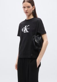 Svart bomulls-T-skjorte med hvit logotrykk, korte ermer og en ledig passform. Kombinert med en liten svart plissert veske.