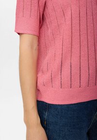 Rosa stickad tröja med korta ärmar, med horisontell ribbad textur och vertikala randdetaljer; bärs över mörka denimjeans.