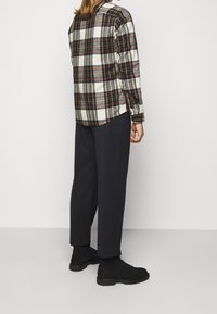 Camicia di flanella a quadri con motivi rossi, verdi e bianchi, abbinata a pantaloni scuri e larghi e stivali neri stringati.