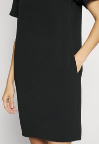 Black dress made of smooth fabric, featuring short sleeves and side pockets. The design is simple and A-line, with a straight hemline.