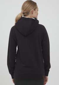 Sudadera con capucha negra, interior suave, puños y dobladillo acanalados. Presenta una capucha de doble capa y una pequeña etiqueta con el logotipo en la parte inferior izquierda.