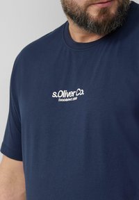 Granatowa bawełniana koszulka z krótkim rękawem i okrągłym dekoltem, z białym logo s.Oliver Co. nadrukowanym na piersi.