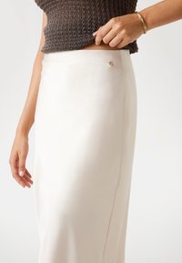 Krämfärgad satin kjol med en elegant design, med en liten silverknappdetalj och en mjuk textur.