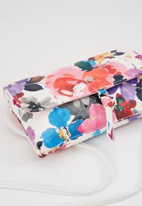 Kopertówka z kolorowym kwiatowym nadrukiem, zamykana na klapę, z małym metalowym detalem i białym paskiem na ramię na białym tle.