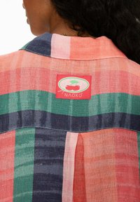 Kockovaná košeľa v mnohých farbách s horizontálnymi pruhmi v ružovej, zelenej a námornej farbe, s červenou etiketou s nápisom "Naoko". Ľahký materiál, voľný strih.