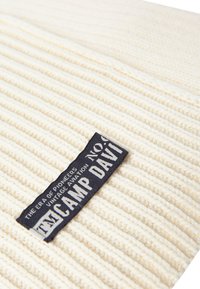 Knitted cream fabric with a ribbed texture; features a dark blue label with white text reading "CAMP DAVID" and additional branding details.