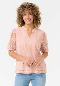 Light pink blouse with a geometric lace design, short puff sleeves, and a V-neckline. The fabric has a delicate texture and openwork details.
