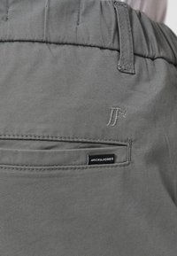 Γκρι παντελόνι από ύφασμα με ελαστική μέση, πίσω τσέπη με ραμμένες λεπτομέρειες και μια μικρή μαύρη ετικέτα με την επιγραφή "JACK & JONES".