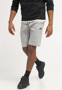 Light grey Nike shorts with an elastic waistband and drawstring, featuring side pockets and a black logo. Paired with black sneakers and socks.