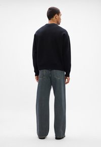 Čierna mikina s okrúhlym výstrihom a rebrovanými manžetami, v kombinácii s voľnými šedými džínsy s bledým dokončením a zadnými vreckami.