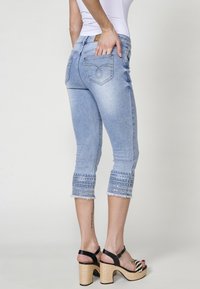 Gai zilgani denim capri bikses ar saplēstu apakšmalu un sarežģītiem rakstu akcentiem pie apkaklēm. Ar aizmugurējām kabatām un vidēja pieauguma dizainu.