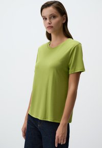 T-shirt verde lime a maniche corte in cotone morbido con scollatura a girocollo, vestibilità rilassata e consistenza liscia, abbinato a jeans blu scuro.