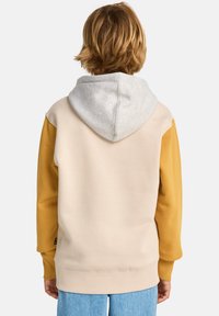 Φούτερ με κουκούλα σε μπεζ χρώμα για το σώμα, μουσταρδί κίτρινα μανίκια και ανοιχτό γκρι κουκούλα. Μαλακό ύφασμα με ριμπ μανσέτες και τελείωμα.