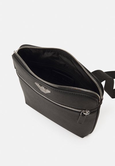 Black leather bag with a textured finish, zipper closure, and silver hardware. Features a logo on the front and a spacious interior.