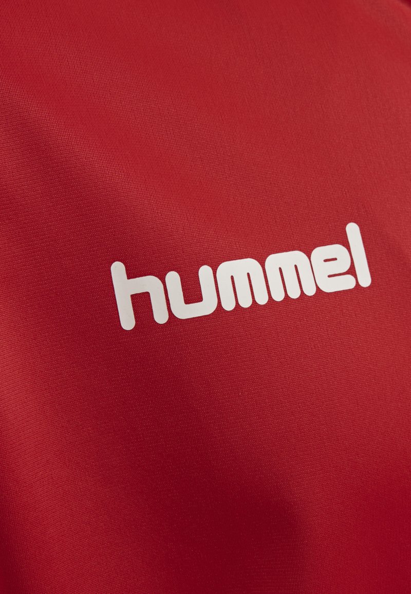 Tissu rouge avec une texture lisse et un logo blanc proéminent qui lit "hummel" dans une police arrondie.