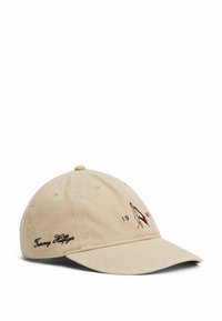 Gorra de béisbol de algodón beige con visera curva. Presenta un logo bordado y "1985" en la parte frontal; "Tommy Hilfiger" está cosido en el lateral.
