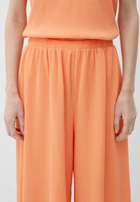 Perzikkleurige plooibroek met wijde pijpen en een elastische tailleband. Soepele, lichte stof met een verticale ribbelstructuur.