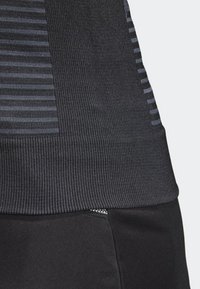 Top atlético negro con textura acanalada y patrones de rayas horizontales en tonos más oscuros. Presenta un diseño ajustado y un acabado suave.