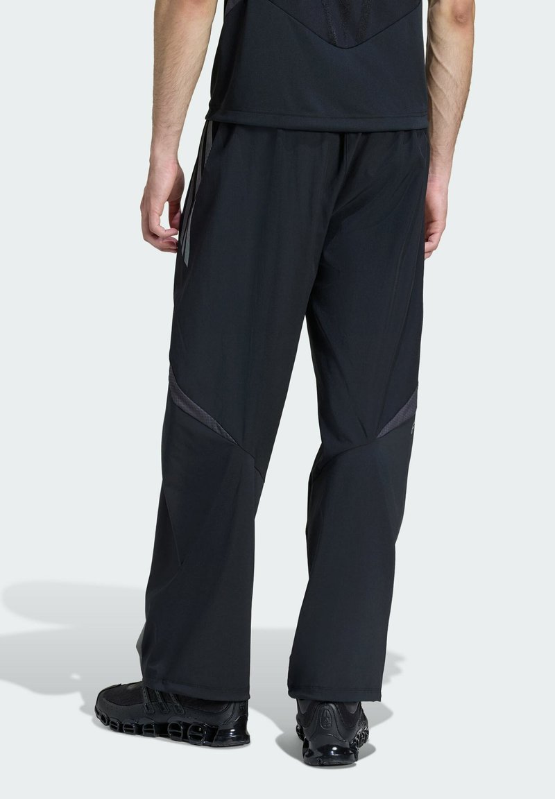 Svarta träningbyxor i lätt tyg, med rakt snitt, nätdetaljer och reflexdetaljer på sidorna. Svarta skor syns.