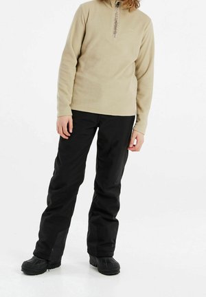 Beiger Fleece-Pullover mit Viertelreißverschluss und Logodetail, kombiniert mit schwarzen wasserdichten Hosen und robustem schwarzen Schuhwerk.