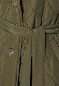 Olive green quilted jacket featuring a belted waist and button closure. The material is smooth with a diamond pattern and soft texture.