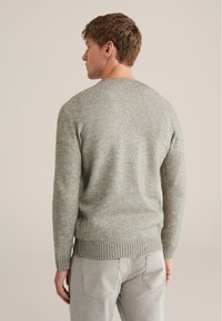 Maglione lavorato a maglia grigio chiaro con un motivo testurizzato, scollo rotondo e polsini e orlo a coste. Modella di spalle, indossa pantaloni chiari.