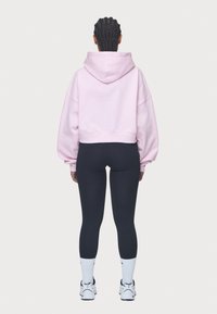 Light pink cropped hoodie with oversized sleeves, paired with black leggings. Model wears white athletic socks and sneakers.