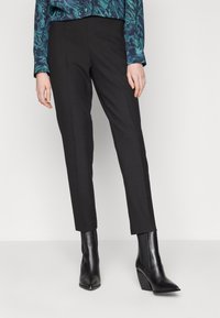 Svarta skräddarsydda byxor med rak passform, med diskreta veck framtill och en slät tygstruktur, ihop med eleganta svarta ankelstövlar.