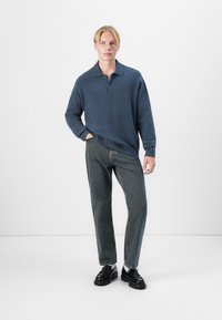 Suéter azul texturizado con cuello, de corte relajado. Combinado con jeans de denim oscuro de pierna recta y mocasines negros. Look sencillo y casual.