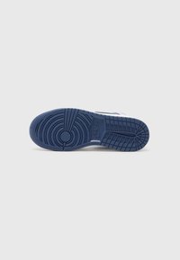 Semelle d'une chaussure de sport Nike bleue avec des motifs circulaires et des rainures rectangulaires sur un fond neutre.