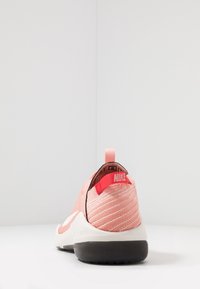 Bakvy av en rosa Nike-sko med en svart sula och röda detaljer, placerad på en vit bakgrund.