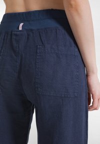Lniane spodnie w kolorze granatowym o luźnym kroju, z szerokim elastycznym pasem i dwoma tylnymi kieszeniami. Teksturowana tkanina z widocznymi przeszyciami.